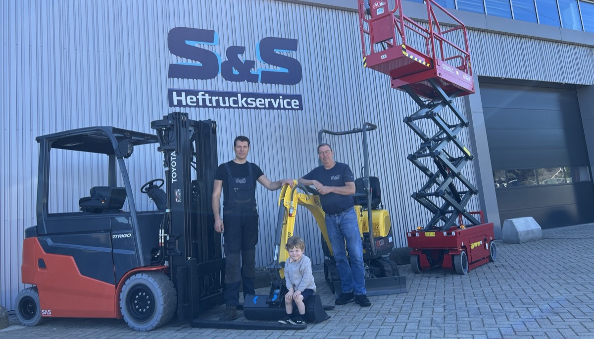 Twee medewerkers van S&S Heftruckservice voor de eigen hal in Maastricht, met een Toyota-heftruck, een minigraver en een schaarhoogwerker